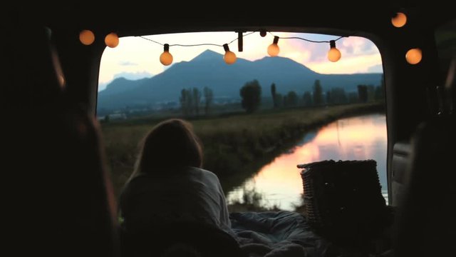A young woman admiring the sunset in the trunk of a car decorated with twinkle lights.