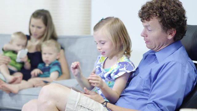 Father and daughter using tablet with family in the living room