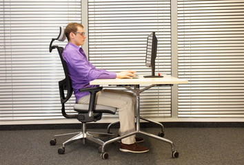 correct sitting position at workstation. man on chair working with pc - obrazy, fototapety, plakaty