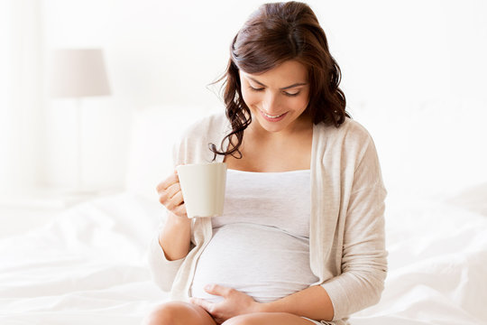 happy pregnant woman with cup drinking tea at home