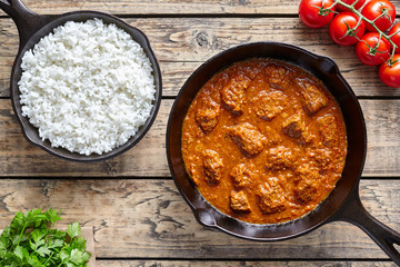 Traditional Beef Madras Indian spicy lamb food with rice in cast iron pan on vintage wooden table background. Delicious India culture restaurant dish.