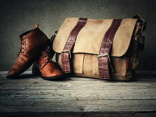 Men's boots and brown bag on wooden table over wall grunge background