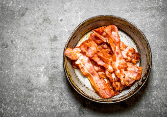 Fried bacon in a frying pan. On stone background.