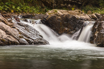 Fototapeta premium Landscape of mountain river in sunshine. View of the stony rapids. Fast jet of water at slow shutter speeds give a beautiful magic effect.