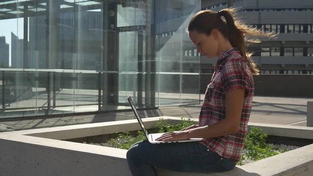 Woman with laptop near the glass facade of the building in downtown