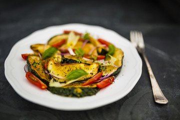 Salad with fried zucchini and tomatoes with herbs served on white plate on stone background .
