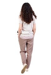 back view of standing young beautiful woman. Long-haired curly girl goes with his hands in his pockets.