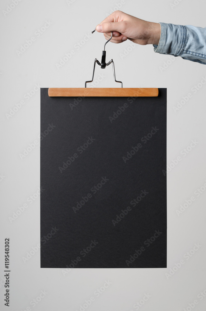 Wall mural Black A3 Poster Mock-Up - Man holding a black poster on a clothes hanger on a white background.