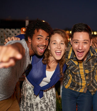 Multi-ethnic millenial friends taking a flash selfie with mobile phone on rooftop patio