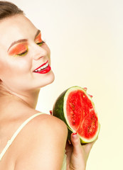 Молодая женщина с красным макияжем глаз и губ искренне улыбается и держит в руках спелый разрезанный арбуз.