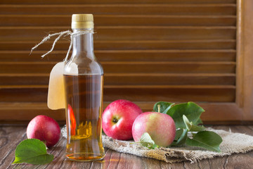 Apple cider vinegar in a glass bottle with fresh apples on a woo