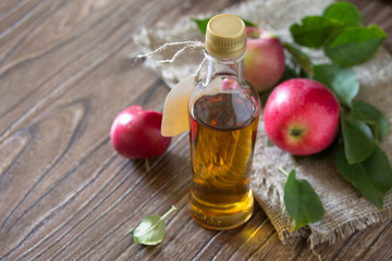 Apple cider vinegar in a glass bottle with fresh apples on a woo