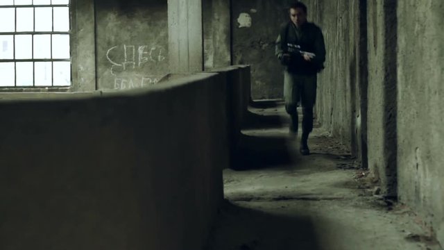 Two armed men in military uniforms were exchanging fire in the hall of an abandoned German factory. During shooting using freeze frame effect.