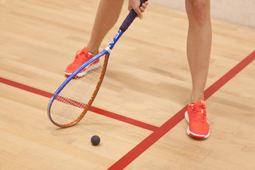 A young female squash player hiting a ball in a squash court