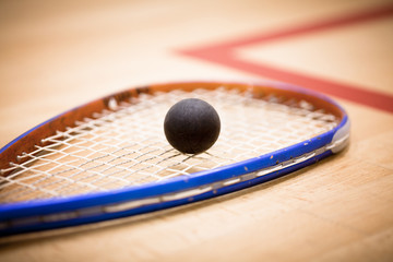 Close up of a squash ball on racket over wooden background - 119550792