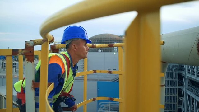 Asian engineer climbing the tower of a large oil refinery