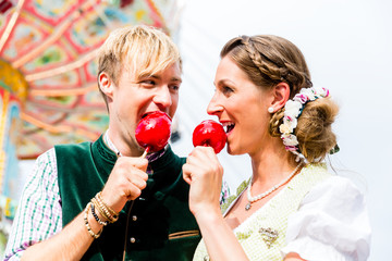 Frau und Mann in bayerischer Tracht beißt in Liebesäpfel vor einem Karussell