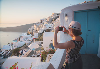 young woman tourist taking photo on mobile phone smartphone in Greece Santorini at sunset