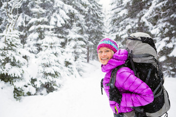 Fototapeta na wymiar Happy woman walking in winter forest with backpack. Girl winter hiking with backpack.