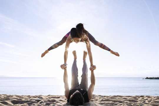 Man lifting woman while doing yoga on beach during summer