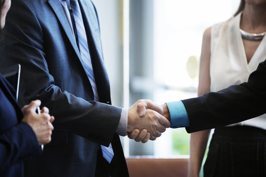Businessmen shaking hands while standing with colleagues in office