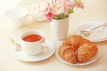 Cup of tea with flowers and croissants on table