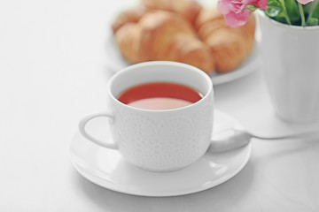 Cup of tea with flowers and croissants on table