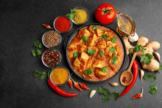 Chicken curry with different spices on dark background