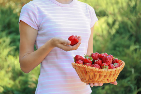 Woman holding wicker basket with fresh strawberries outdoor
