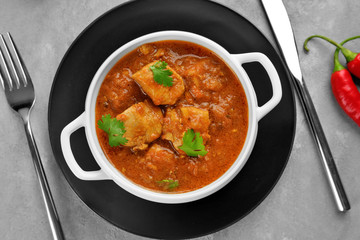 Tasty chicken curry in soup plate on grey background