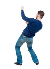 back view of standing man pulling a rope from the top or cling to something. bearded man in blue pullover pulls a rope from the top.