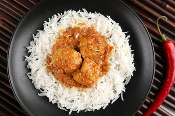 Tasty dinner with chicken curry and rice in plate on bamboo background