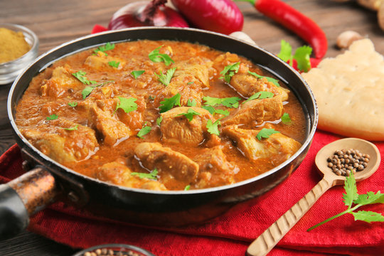 Tasty chicken curry in pan and spices on wooden background