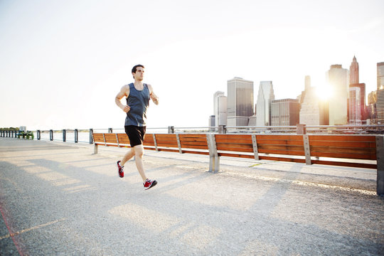 Man running by bench at riverbank against clear sky on sunny day