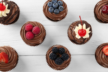 Delicious chocolate cupcakes with berries on white table, top view