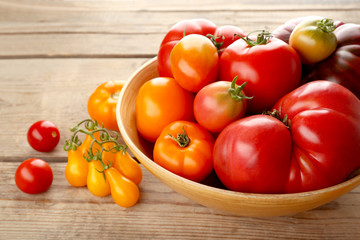 Bowl with red and yellow tomatoes on wooden background