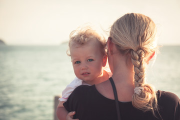 Child with a sincere look hugging his mother sitting on her hands and looking at camera. Mother...