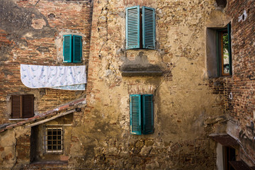 dans un village toscan, des fenêtres aux volets verts avec un drap tendu