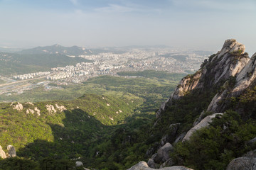 Fototapeta na wymiar View of the city far away from above and steep granite peaks of Jaunbong Peak on Dobongsan Mountain at the Bukhansan National Park in Seoul, South Korea.