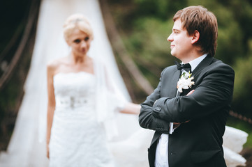 Bride and groom in wedding dresses on the river bridge. Mountain river. Just married couple on the suspension bridge over the river