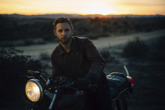 Portrait of man riding motorcycle on field during sunset