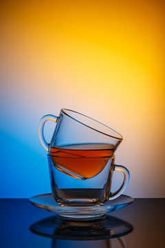 Two 

transparent glass cups . In the upper Cup of tea. The Cup and saucer. The Studio photos. The rear 

light. The reflection on the table. On a black table. Background blue orange.