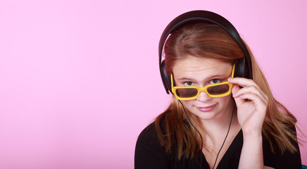 Redhead teen with headphones and yellow sunglasses on pink