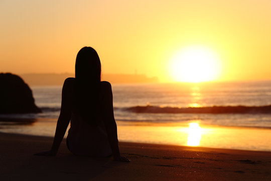 Woman silhouette watching sun at sunset