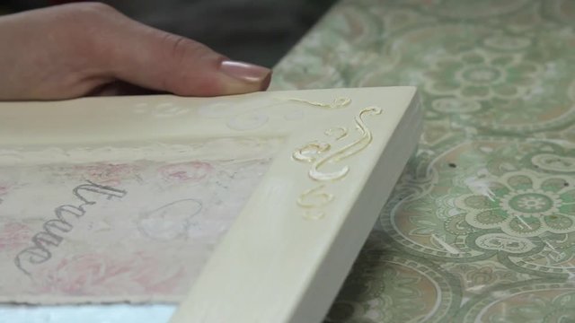 The girl draws ornament gold paint on a wooden frame