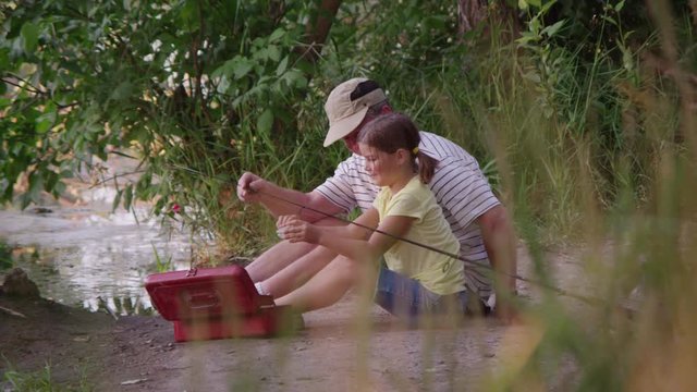 Grandfather teaching granddaughter how to fish and bait