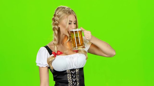 Girl in bavarian national costume drinks beer and shows thumb. Green screen