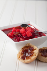 Homemade borscht vegetable beet soup with homemade whole wheat rolls topped with pluot jam vertical shot on white wood