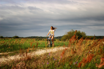 Young beautiful woman rides a bicycle in the summer next to the green fields stretched out hand in the air. Soft and blur conception