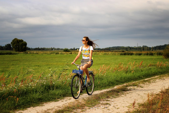 Young beautiful woman rides a bicycle in the summer next to the green fields stretched out hand in the air. Soft and blur conception